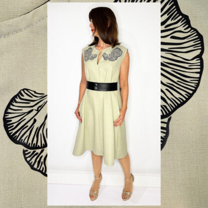 Light green sleeveless dress with Djamoer Barat print, featuring a vegan black belt, side-seam pockets, and black bias tape finishing.