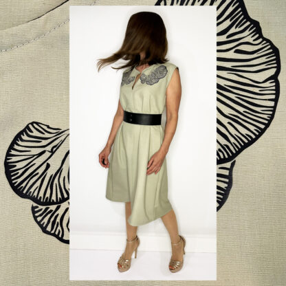 Light green sleeveless dress with Djamoer Barat print, featuring a vegan black belt, side-seam pockets, and black bias tape finishing.