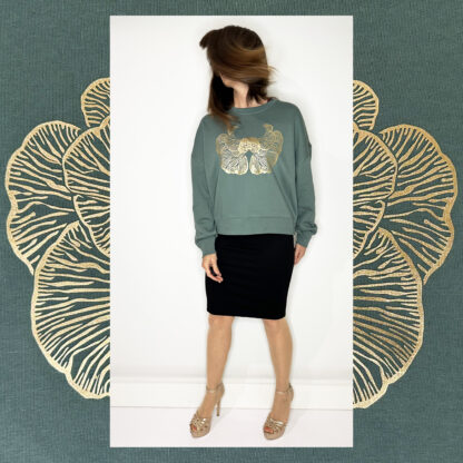 A moss-green sweater with a golden print of the Djamoer Barat mushroom from Sumatra, featuring a roomy and slightly cropped fit. Made of 100% organic cotton, Fairwear-certified, and handprinted in Studio Catta’s boutique atelier in Amsterdam, showcasing sustainable fashion.