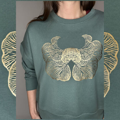 A moss-green sweater with a golden print of the Djamoer Barat mushroom from Sumatra, featuring a roomy and slightly cropped fit. Made of 100% organic cotton, Fairwear-certified, and handprinted in Studio Catta’s boutique atelier in Amsterdam, showcasing sustainable fashion.