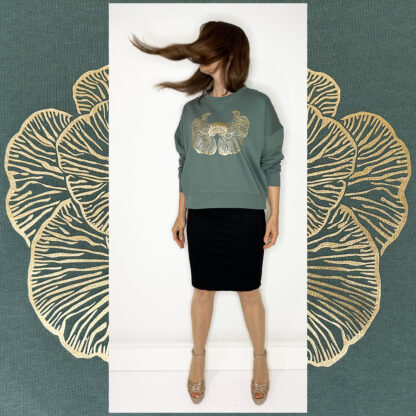 A moss-green sweater with a golden print of the Djamoer Barat mushroom from Sumatra, featuring a roomy and slightly cropped fit. Made of 100% organic cotton, Fairwear-certified, and handprinted in Studio Catta’s boutique atelier in Amsterdam, showcasing sustainable fashion.