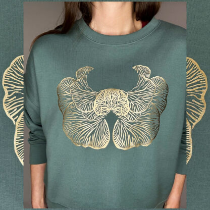 A moss-green sweater with a golden print of the Djamoer Barat mushroom from Sumatra, featuring a roomy and slightly cropped fit. Made of 100% organic cotton, Fairwear-certified, and handprinted in Studio Catta’s boutique atelier in Amsterdam, showcasing sustainable fashion.