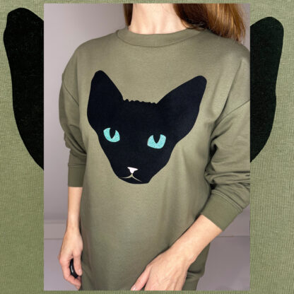 Forest green long sweater featuring a unique cat print in black velvet foil with glittering green eyes, made from organic cotton and Fair Wear-certified, hand-printed in Amsterdam.