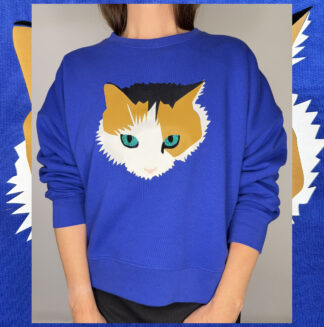 Electric-blue organic cotton sweatshirt with hand-printed calico cat design and green glitter eyes, slightly cropped with dropped shoulders, made by Studio Catta in Amsterdam.